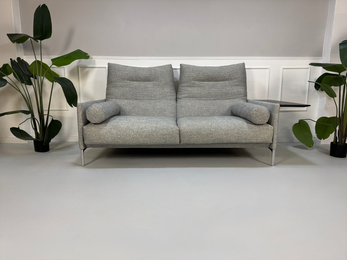 Gebrauchtes graues Stoffsofa mit einem Hocker von COR Modell Avalanche vor einer modernen Wand.