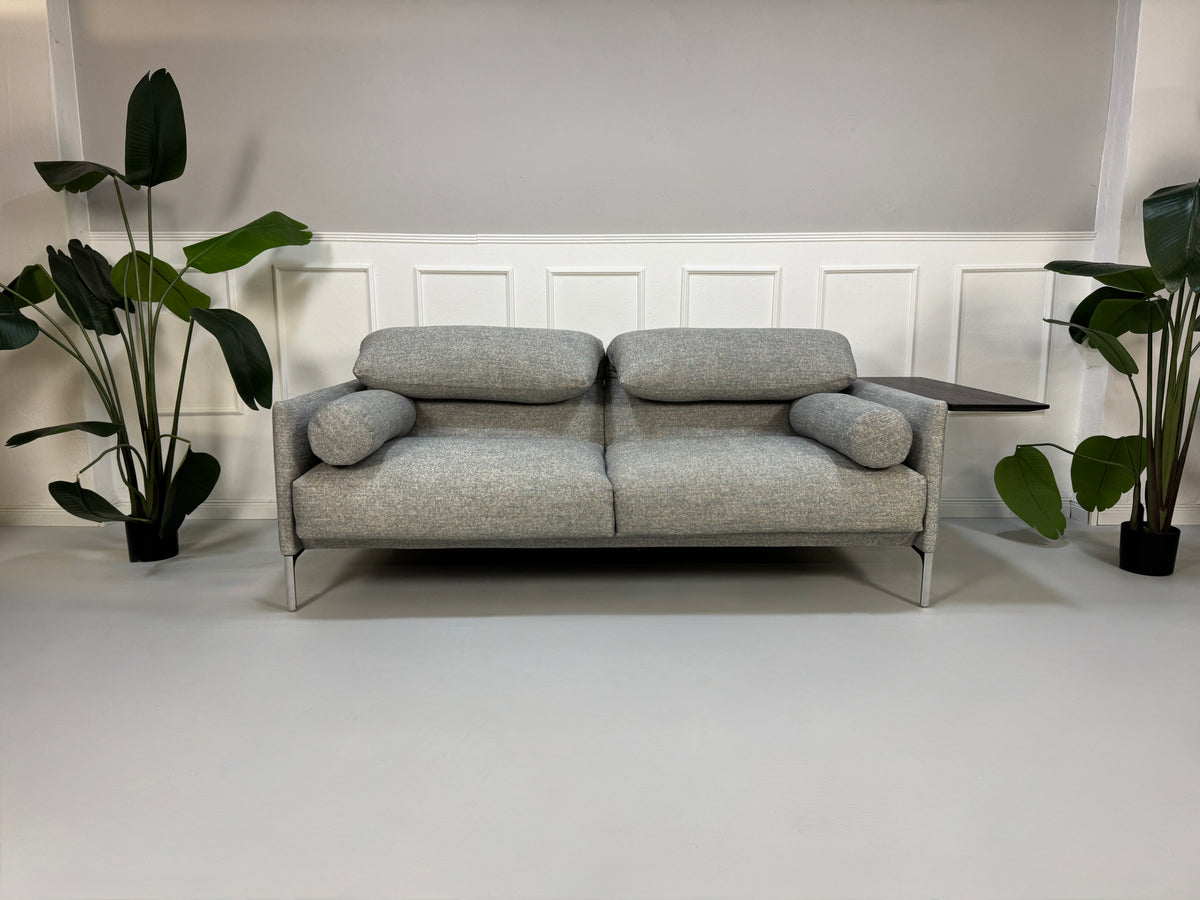 Gebrauchtes graues Stoffsofa mit einem Hocker von COR Modell Avalanche vor einer modernen Wand.