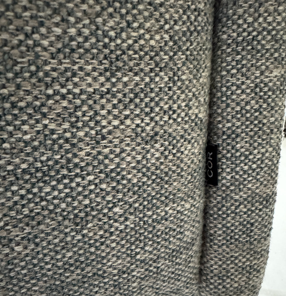 Gebrauchtes graues Stoffsofa mit einem Hocker von COR Modell Avalanche vor einer modernen Wand.