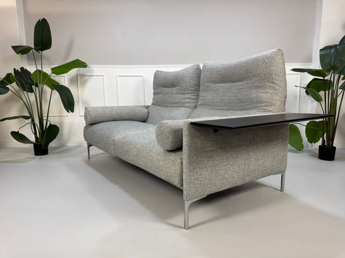 Gebrauchtes graues Stoffsofa mit einem Hocker von COR Modell Avalanche vor einer modernen Wand.