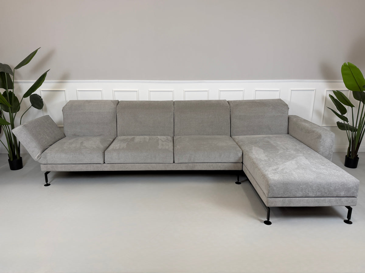 Gebrauchtes graues Brühl Moule Designer Stoff Ecksofa vor einer Wand, stilvoll und modern eingerichtet.