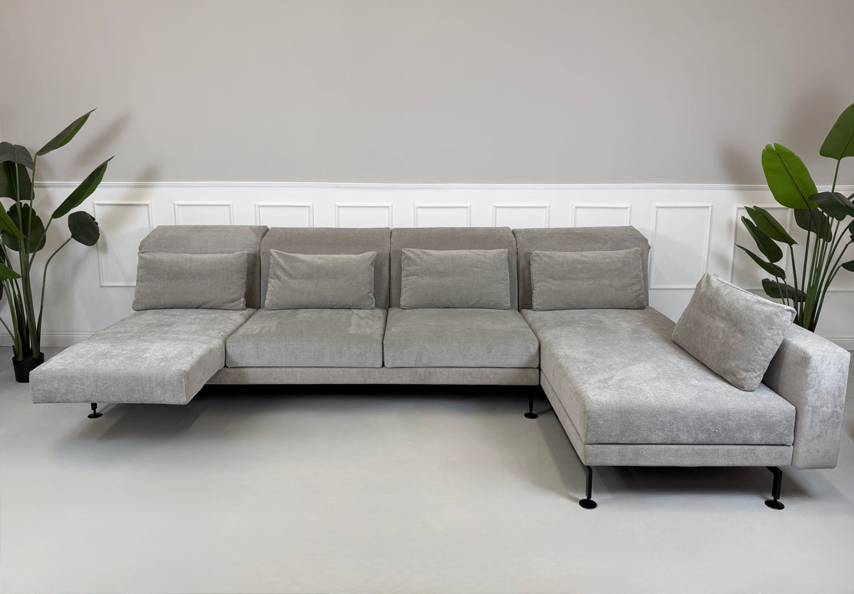 Gebrauchtes graues Brühl Moule Designer Stoff Ecksofa vor einer Wand, stilvoll und modern eingerichtet.
