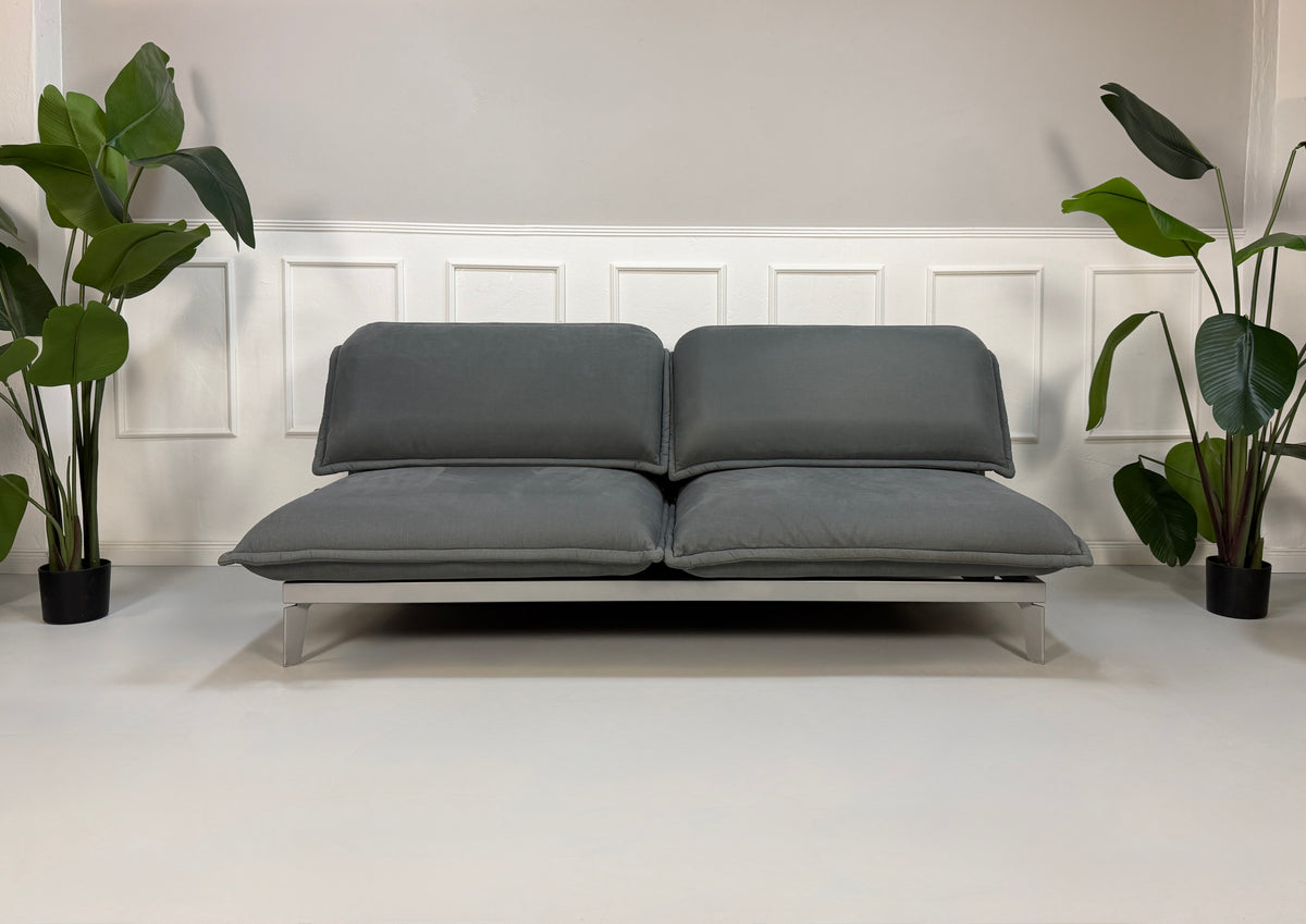 Gebrauchtes graues Rolf Benz Nova Designer Stoff Sofa vor einer Wand, stilvoll und modern eingerichtet.