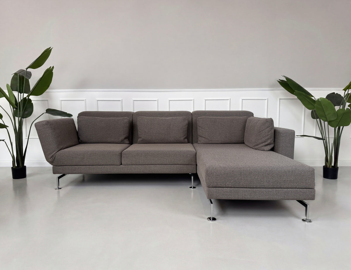 Gebrauchtes braun-graues Brühl Moule Designer Stoff Ecksofa vor einer Wand, stilvoll und modern eingerichtet.