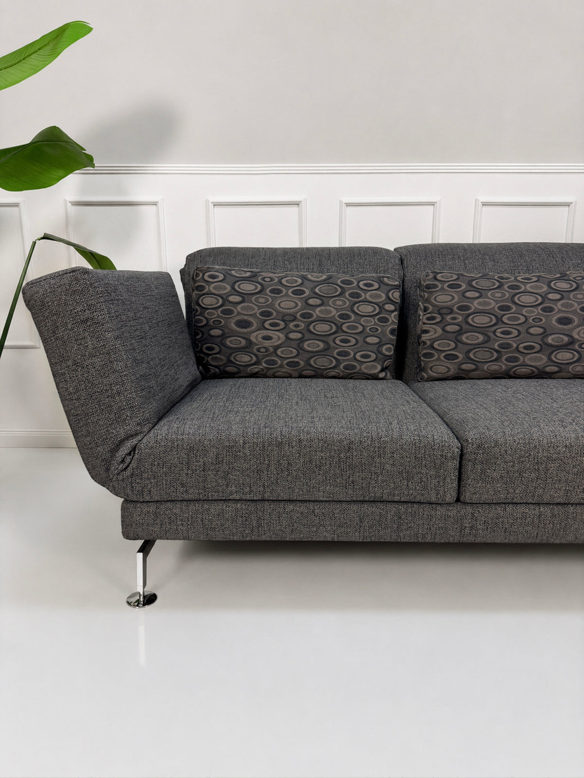 Gebrauchtes graues Brühl Moule Designer Stoff Sofa vor einer Wand, stilvoll und modern eingerichtet.