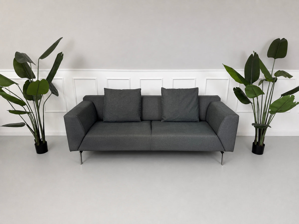 Gebrauchtes graues Rolf Benz 318 Linea Designer Stoff Sofa mit Hocker vor einer Wand, stilvoll und modern eingerichtet.