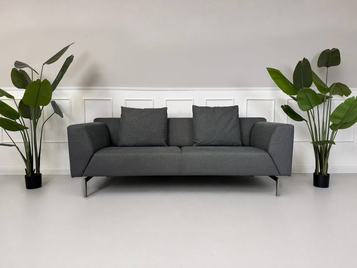 Gebrauchtes graues Rolf Benz 318 Linea Designer Stoff Sofa mit Hocker vor einer Wand, stilvoll und modern eingerichtet.