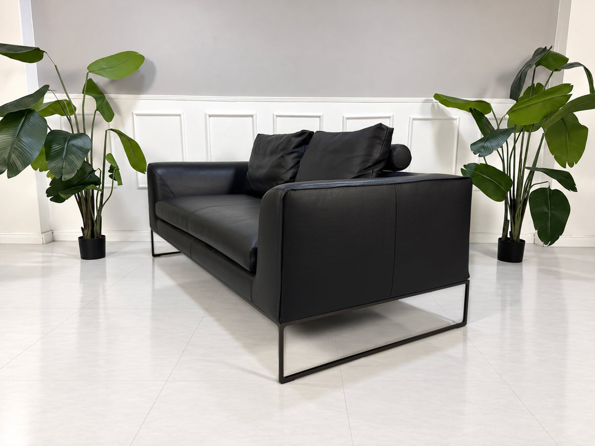 Gebrauchtes schwarzes COR Mell Designer Leder Sofa vor einer Wand, stilvoll und modern eingerichtet.