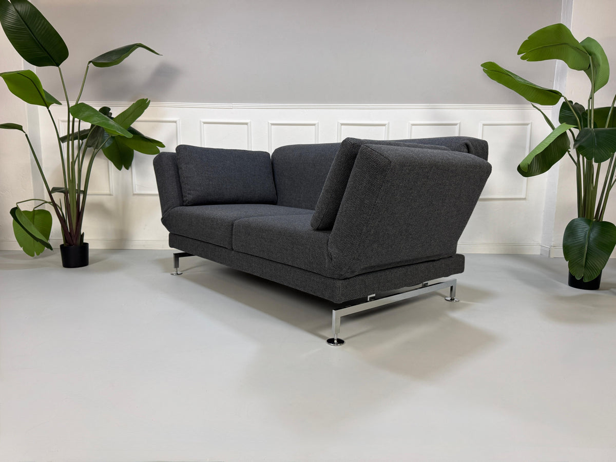 Gebrauchtes graues Brühl Moule Designer Stoff Sofa vor einer Wand, stilvoll und modern eingerichtet.