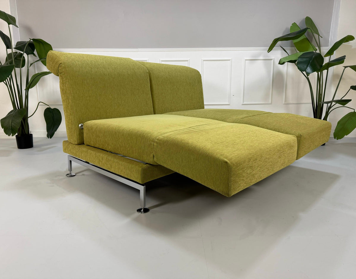 Gebrauchtes grünes Brühl Moule Designer Stoff Sofa vor einer Wand, stilvoll und modern eingerichtet.