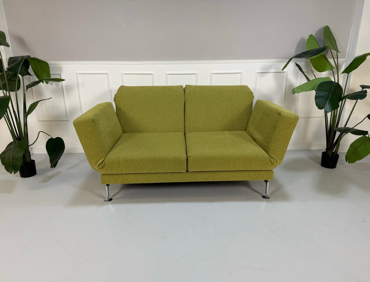 Gebrauchtes grünes Brühl Moule Designer Stoff Sofa vor einer Wand, stilvoll und modern eingerichtet.