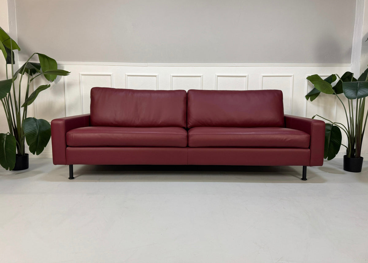 Gebrauchtes rotes COR Conseta Designer Leder Sofa vor einer Wand, stilvoll und modern eingerichtet.