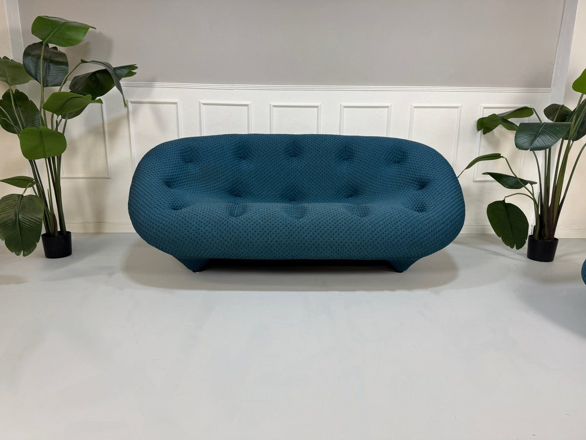 Gebrauchtes blaues Ligne Roset Ploum Designer Stoff Sofa mit Hocker vor einer Wand, stilvoll und modern eingerichtet.
