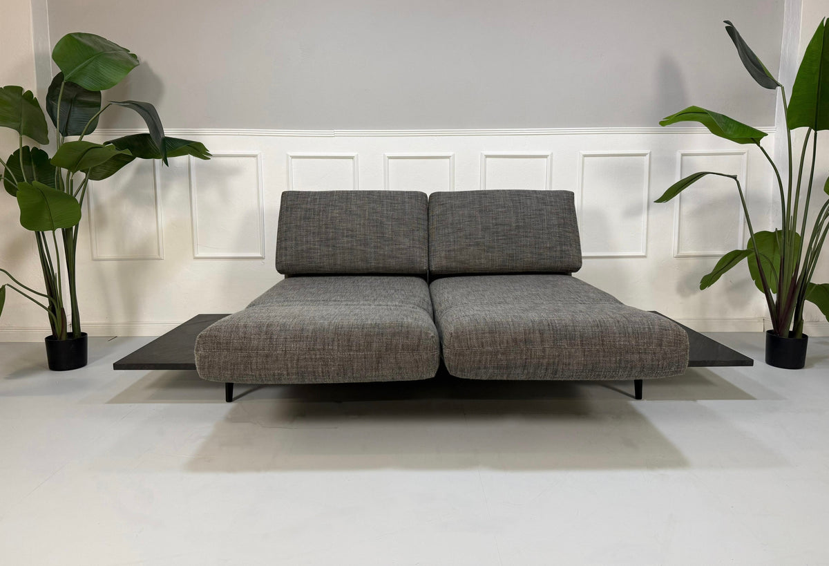 Gebrauchtes graues Rolf Benz Aura Designer Stoff Sofa vor einer Wand, stilvoll und modern eingerichtet.