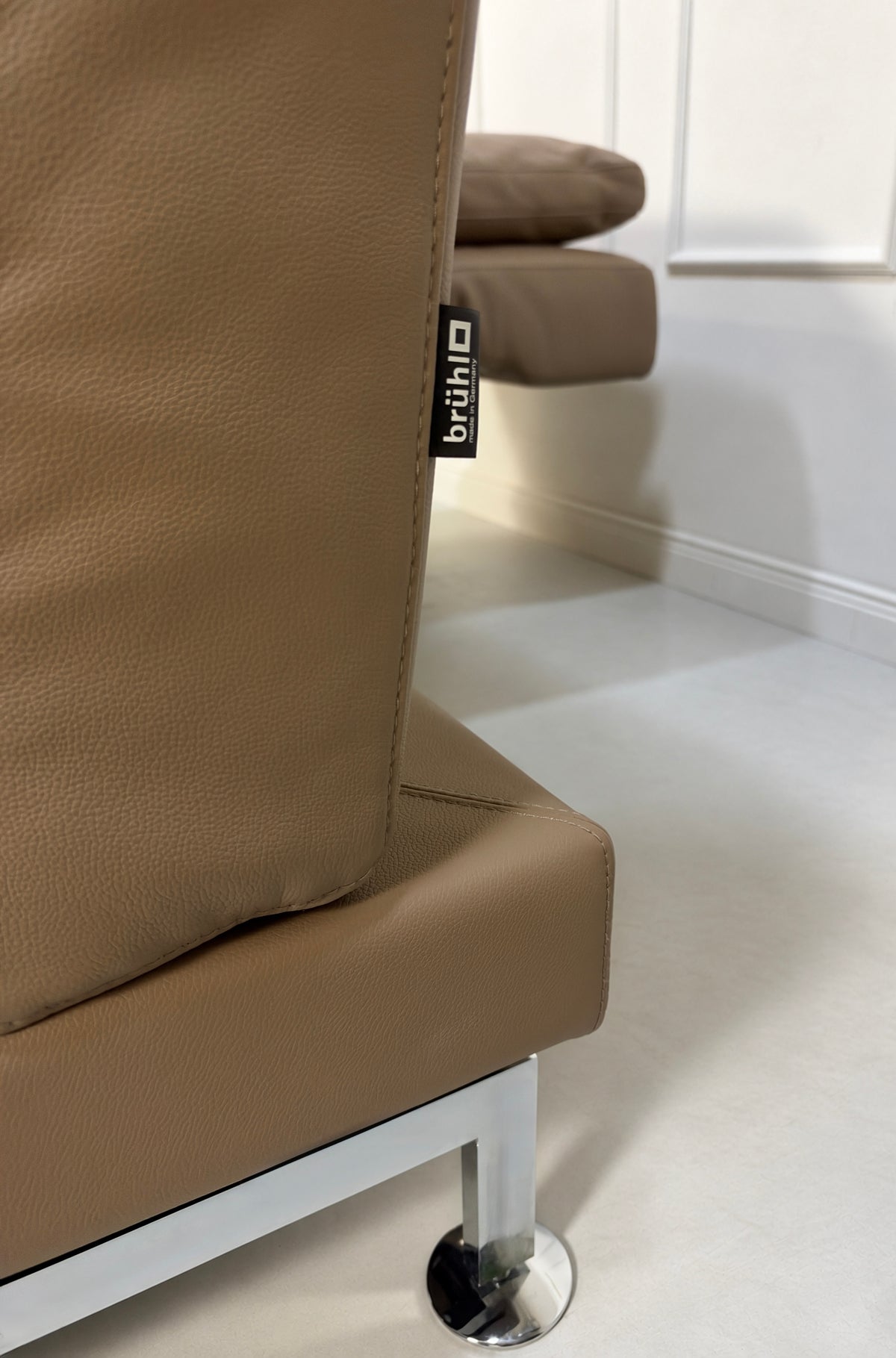 Gebrauchtes braunes Brühl Moule Medium Designer Leder Sofa vor einer Wand, stilvoll und modern eingerichtet.